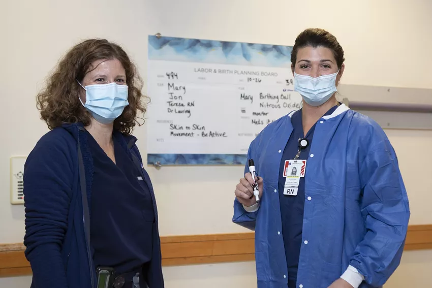 A doctor with a patient, both wearing surgical masks, standing near Labor and Birth Planning Board