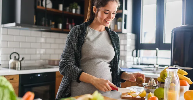 A glowing pregnant woman prepares a healthy meal with fruits and vegetables.