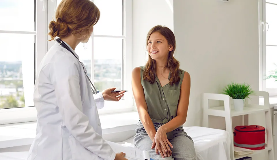A caregiver speaks with a patient sitting on a bed.