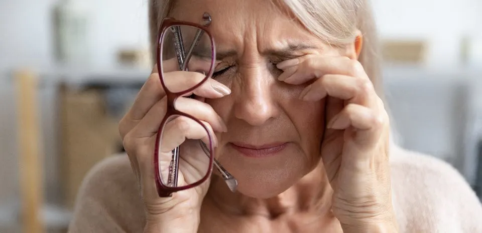 A mature woman holds her glasses and rubs her eyes.