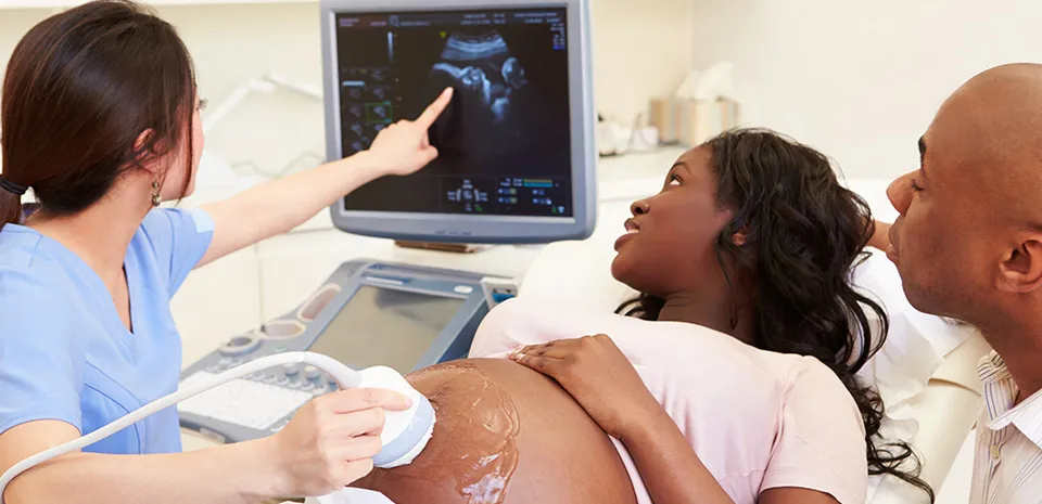 A health care professional is using an ultrasound machine to show an expecting couple an image of their baby on the monitor. 