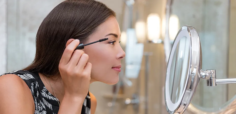 woman looking in mirror putting mascara on