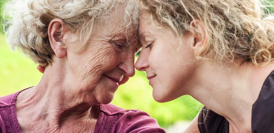 A grandmother and her granddaughter lean into each other, foreheads touching.