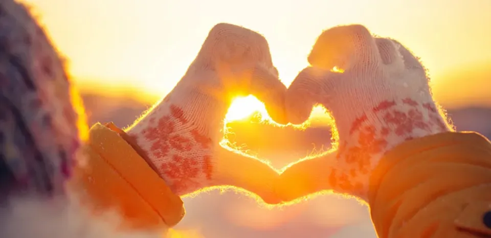 two hands making a heart shape towards towards in the sun in the winter time
