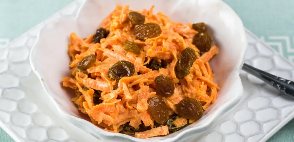 carrot and raisin slaw in a white serving bowl