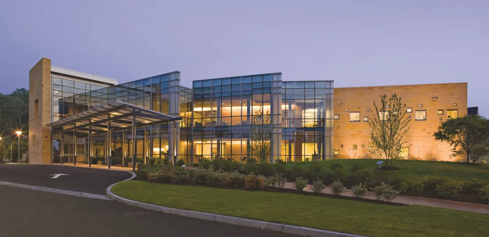 The Cancer Center at night. The front of the building features many glass panes while the lights are on inside.