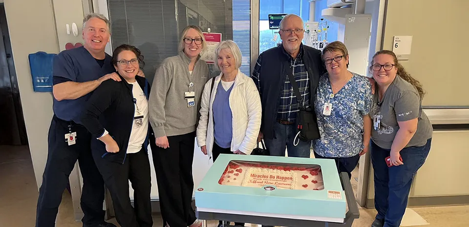 Donald "Jeff" Lawrence poses in front of the large cake he brought to visit the LVAD Program and cardiac care teams who helped him to recover after surgery.