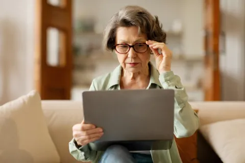 older woman with cataracts wearing glasses struggling to look at a computer.