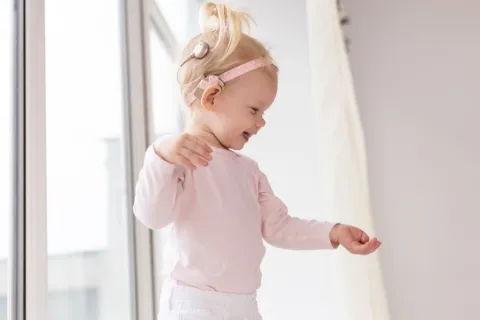 Toddler girl with cochlear implant smiling as she is discovering the world around her