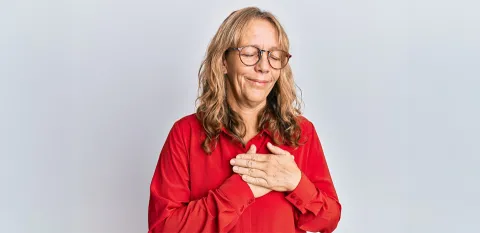 A woman has her eyes closed and both hands placed over her heart.