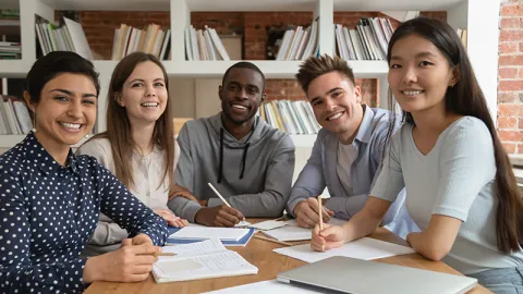 Group of diverse smiling student interns sitting at a desk with a laptop and notepads