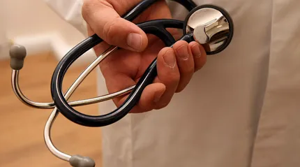 A doctor's hand with a stethoscope in front of his white jacket.