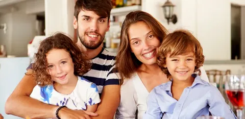 Two children sit on their parents' laps, all with big smiles, at an outdoor dining table