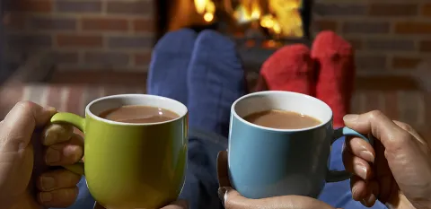 two people drinking hot chocolate by the fireplace