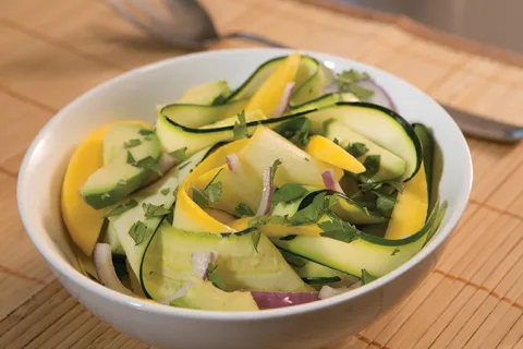 A white bowl is full of yellow and green zucchini noodles.