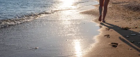 Water is reflecting off the water on a sandy beach, where someone is walking.