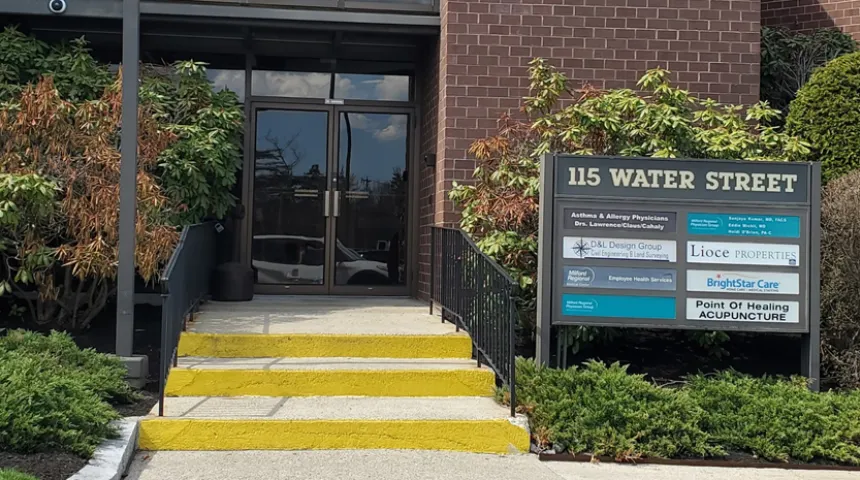 The exterior of a brick building on a sunny day. The steps up are yellow. A sign reads "115 Water Street" and lists the businesses inside.