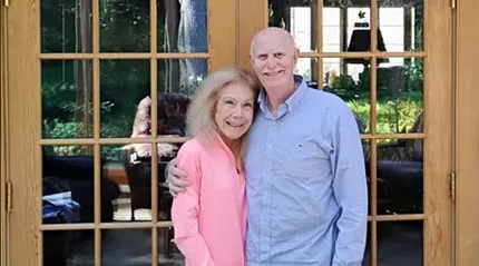 Mitch Grosky, with his arm around his wife, Anne, pose in front of the glass doors to a patio.