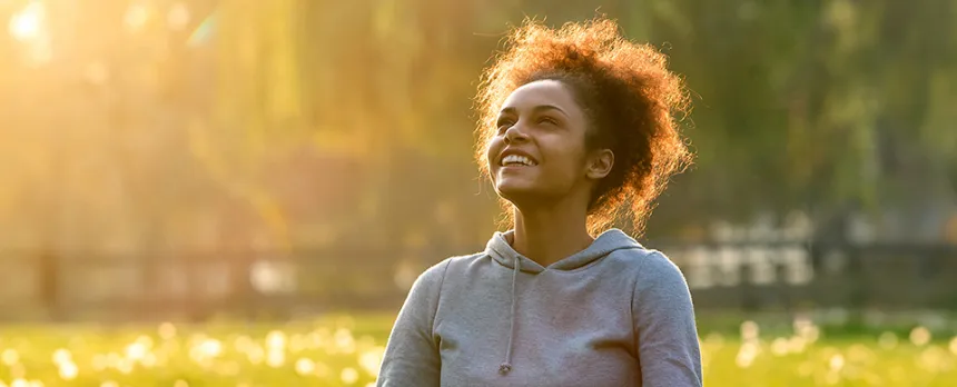 A woman sits in a sunny field appreciating nature and living in the present.
