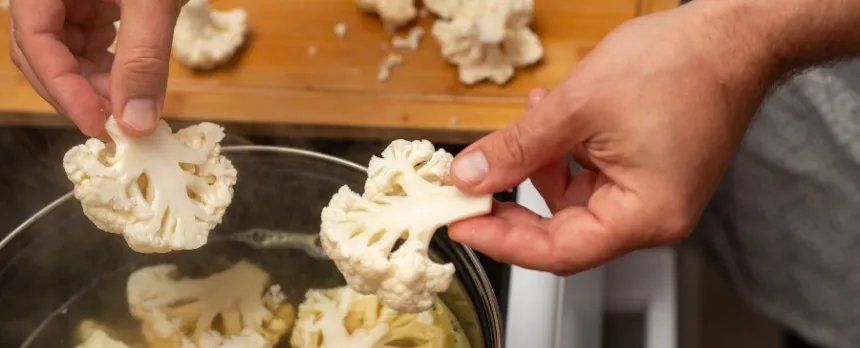 man's hands placing chopped cauliflower into a pot on the stove