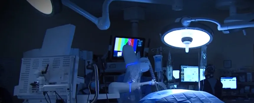 A dark operating room with someone seated in front a a computer screen in the background.