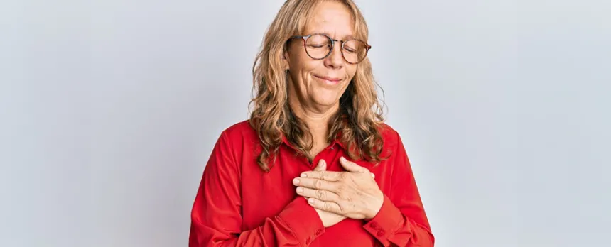 A woman has her eyes closed and both hands placed over her heart.