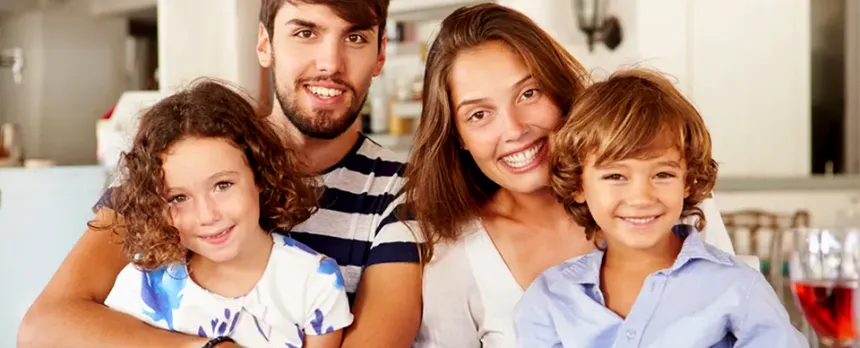 Two children sit on their parents' laps, all with big smiles, at an outdoor dining table