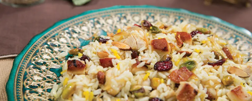 A colorful teal and gold plate holds a rice dish with barberries.