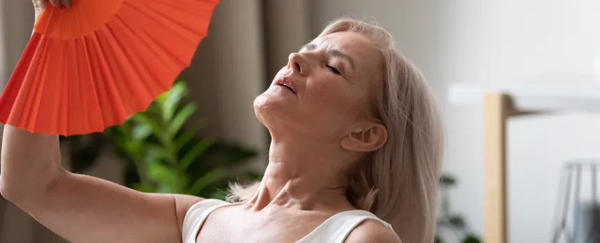 A mature woman is fanning herself with a red hand fan.